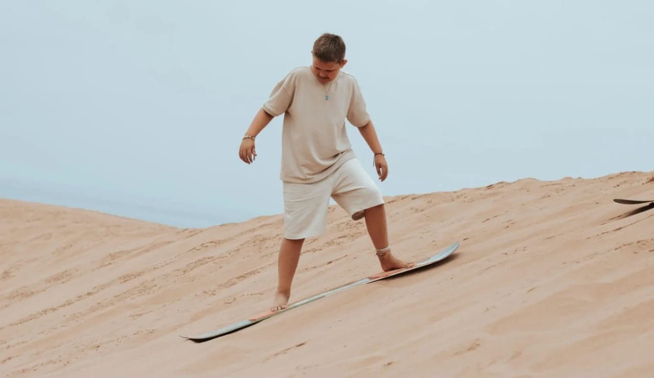 Young rider balancing on a sandboard while sliding down a Timlalin dune